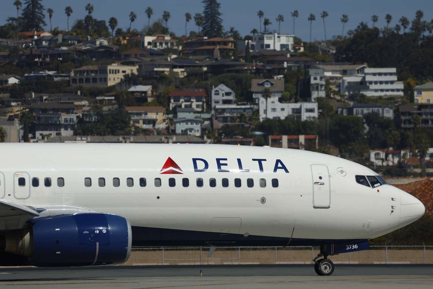 A Delta Air Lines plane is seen on the runway at San Diego International Airport, with houses in the background..