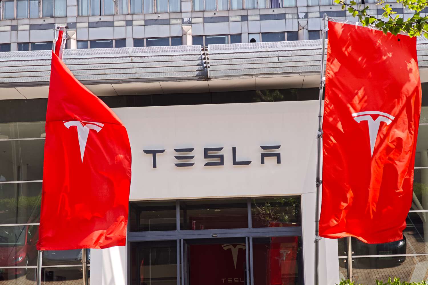 The Tesla logo is seen on banners in front of a dealership building.