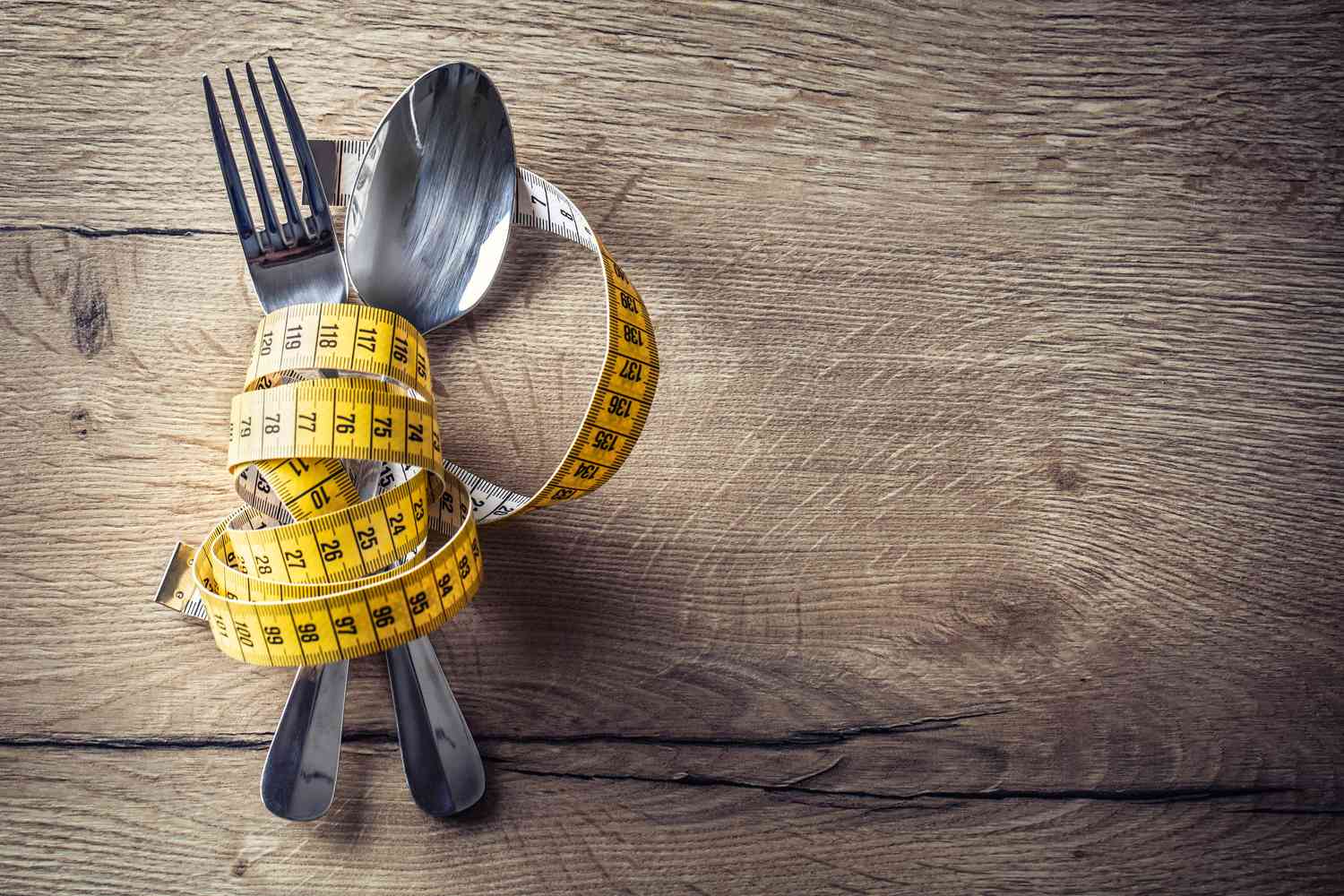 Fork and spoon wrapped in tape measure on table.