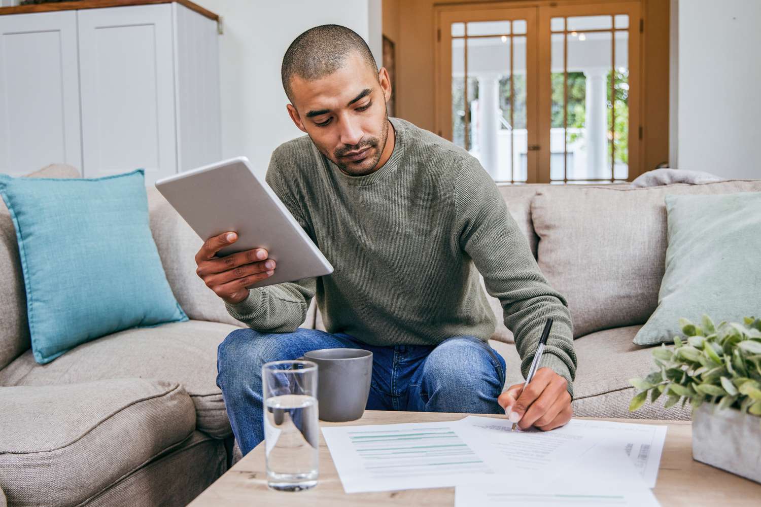 A person doing online banking on tablet while filling out papers.