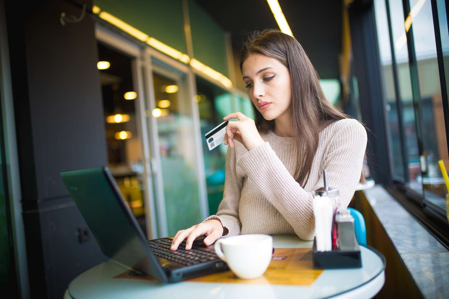 A person holding new credit card just got approved to shop online using a laptop at a cafe.