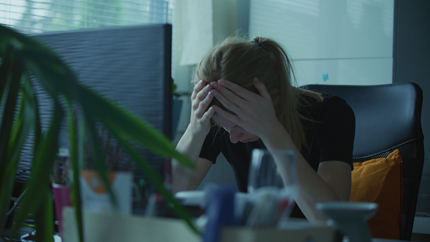 A stock image of a woman holding her head in her hands while at work. 