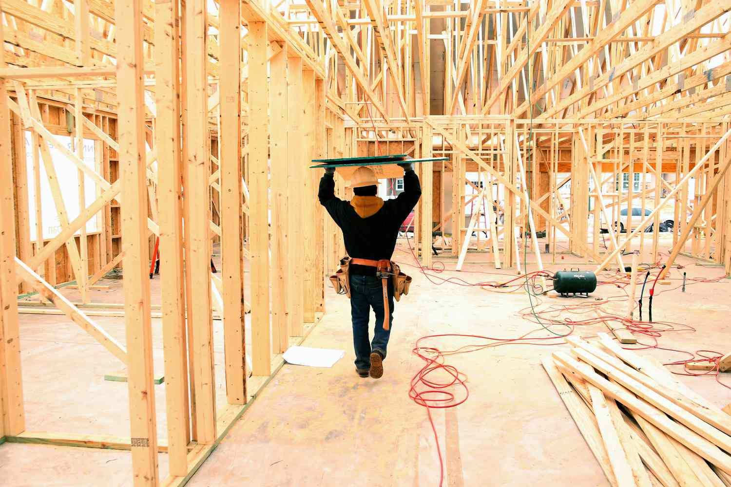 A contractor carries boards through a house under construction 