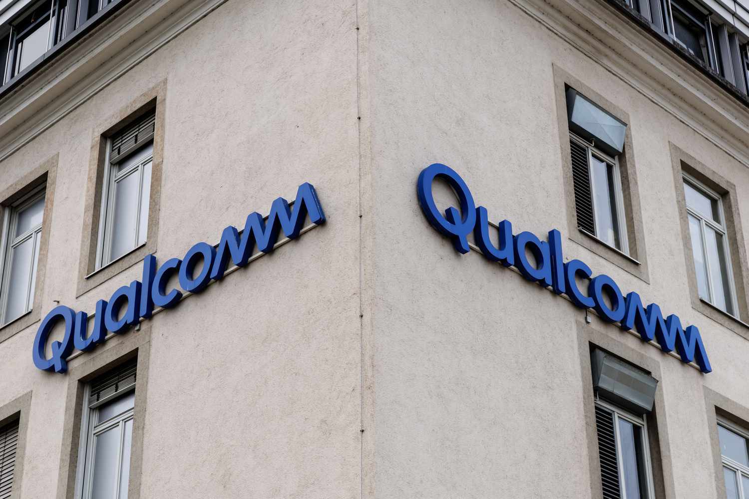 The blue Qualcomm logo is seen on two sides of a tan building.