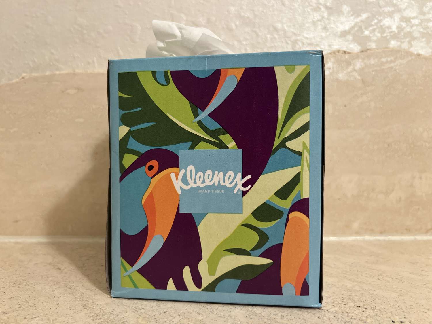 A blue, green, and orange Kleenex box sits on a counter.
