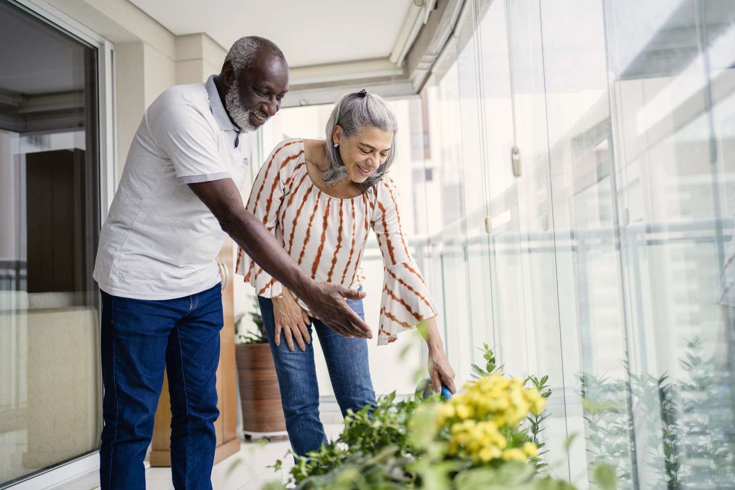 Senior couple taking care of the plants on their balcony in the condo they're planning to use for reverse mortgage.