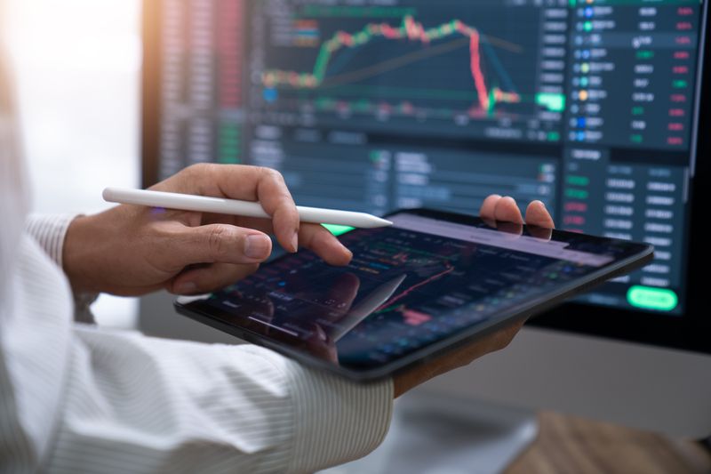 Person holding a tablet in front of a desktop monitor displaying a chart, apple pen in hand