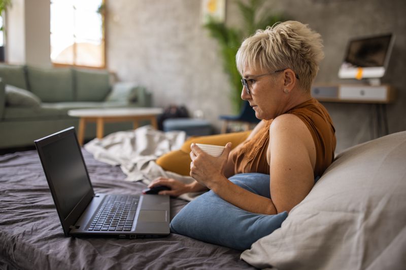 Woman lying on a bed, looking at a laptop computer.