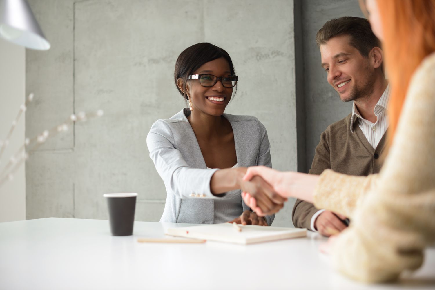 Two people shake hands in an office setting.