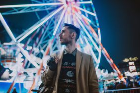 Stylish Young Man at a Carnival/Funfair Standing in Front of a Big Wheel