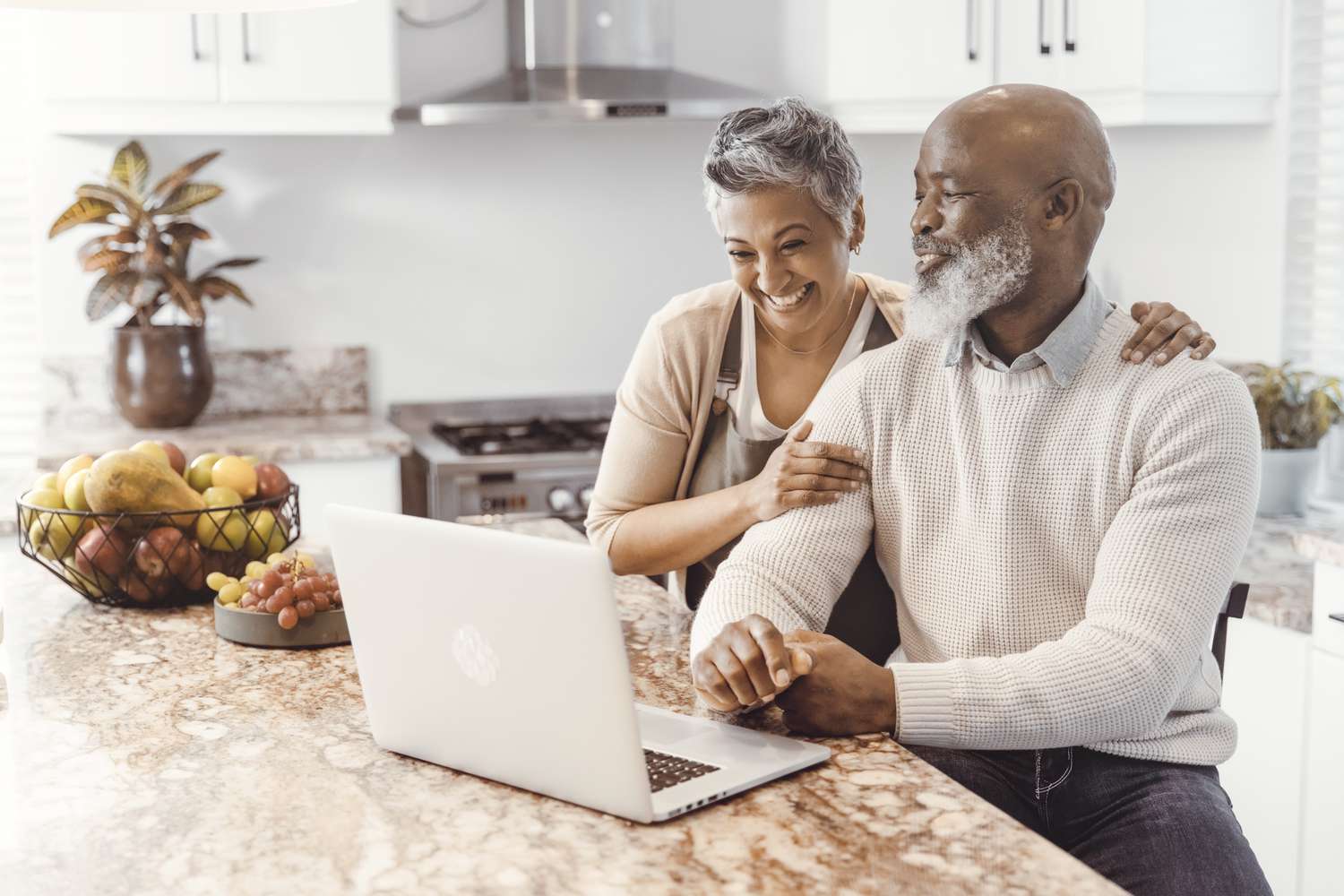 A couple smiling together as they use a laptop in a kitchen