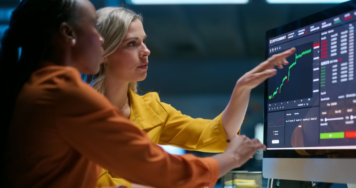 Two analysts look at a computer monitor showing a stock price that has remained unchanged for an extended period.