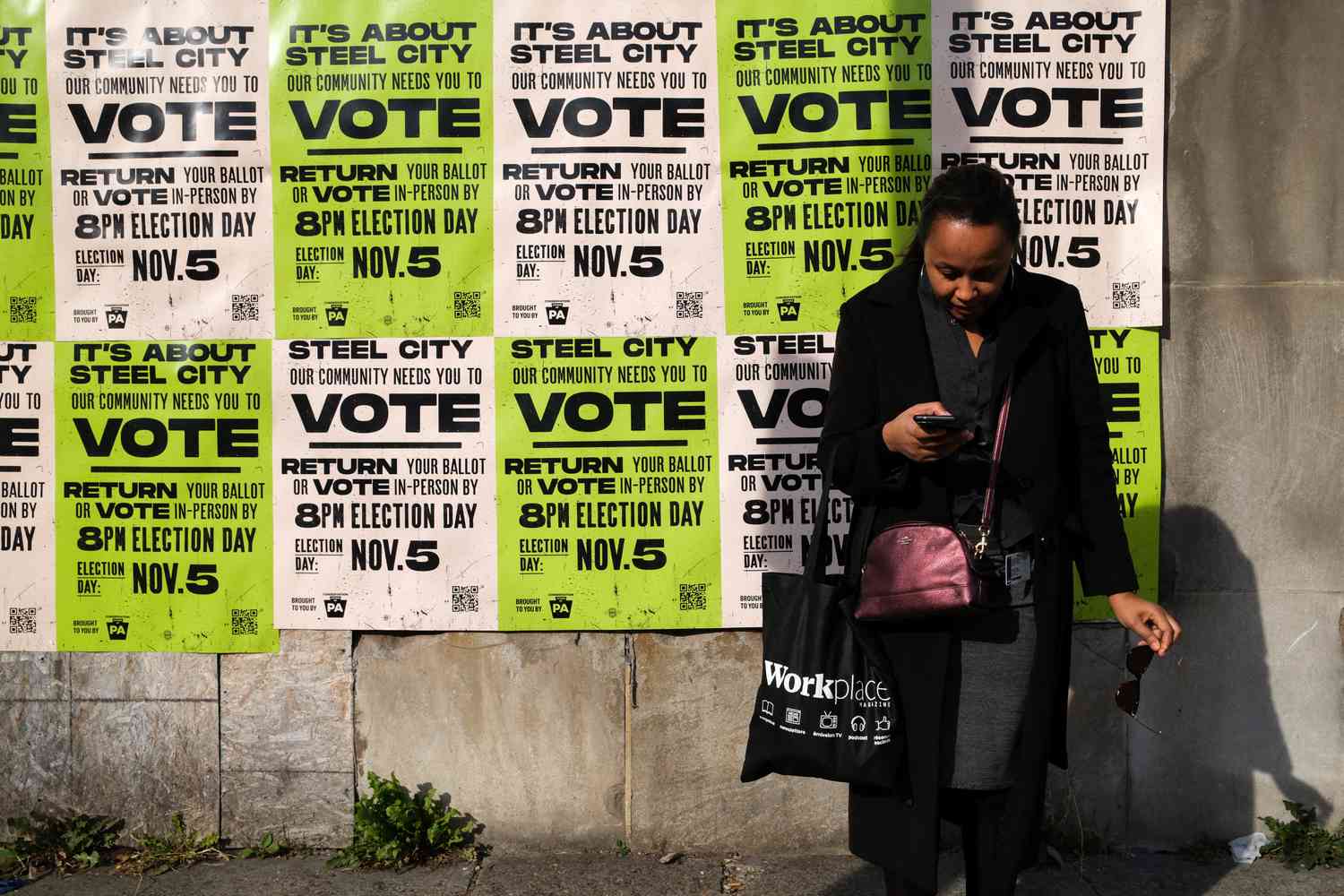 A woman waits for the bus before a wall covered with posters encouraging people to vote in Pittsburgh, Pennsylvania, on November 4, 2024, one day before the US presidential election. 