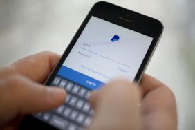 Person holding a mobile phone showing a PayPal account login page.
