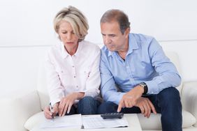 Couple in their 50s or 60s sitting on their sofa and looking at mortgage documents and a calculator