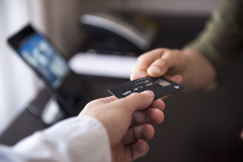 Close-up of person’s hand as they hand a credit card to another person in an office setting