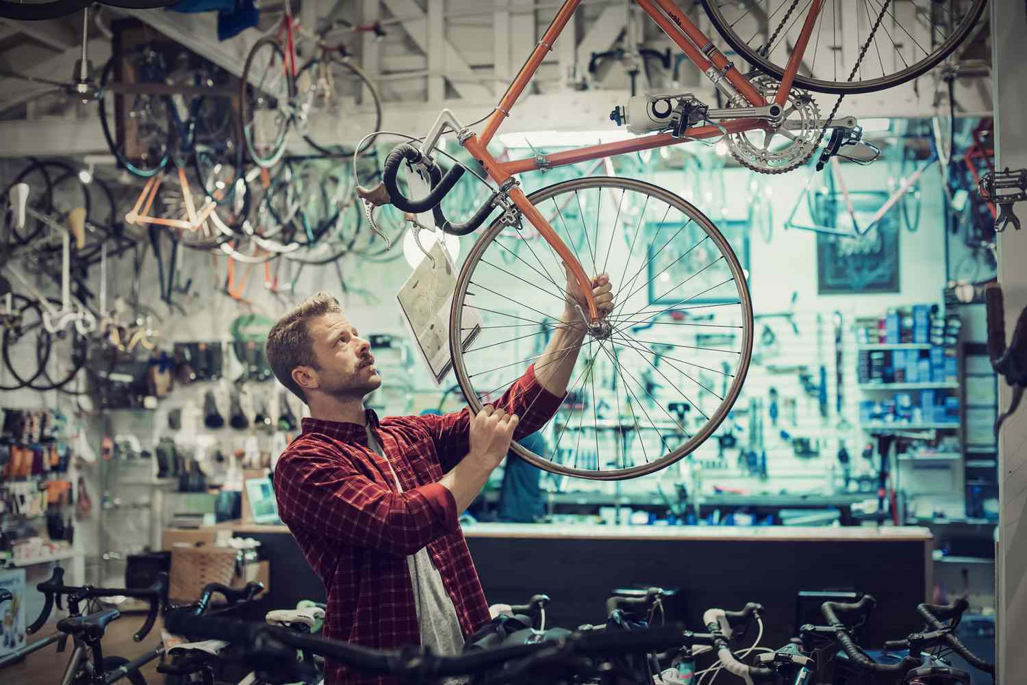 A bike shop owner shifts the front wheel of a display bicycle that is suspended from the ceiling of a narrow store overflowing with new bicycles.