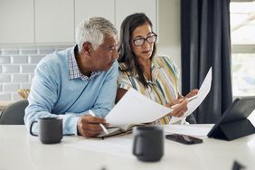 An older couple is sitting at their kitchen table reviewing financial documents.