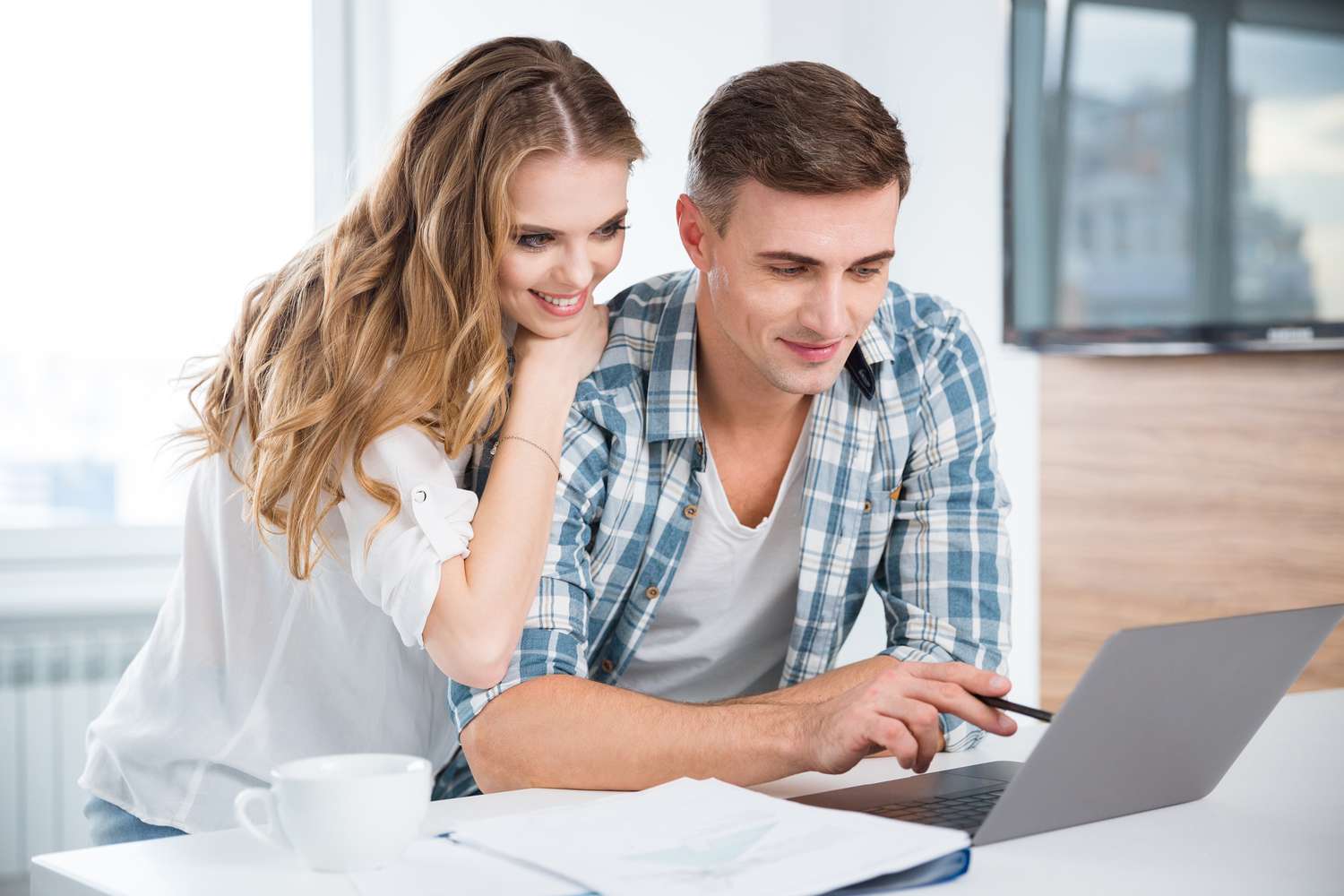 Young couple at their kitchen counter, looking happily together at a laptop