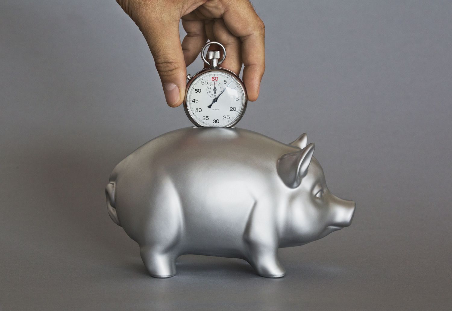 A stopwatch on top of a piggy bank