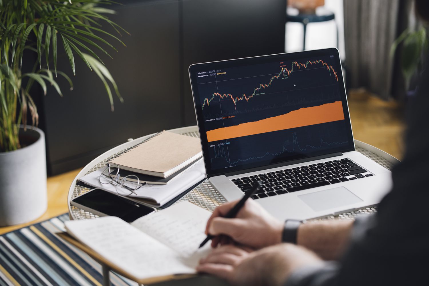 Man making notes while studying a chart on a laptop on a desk.