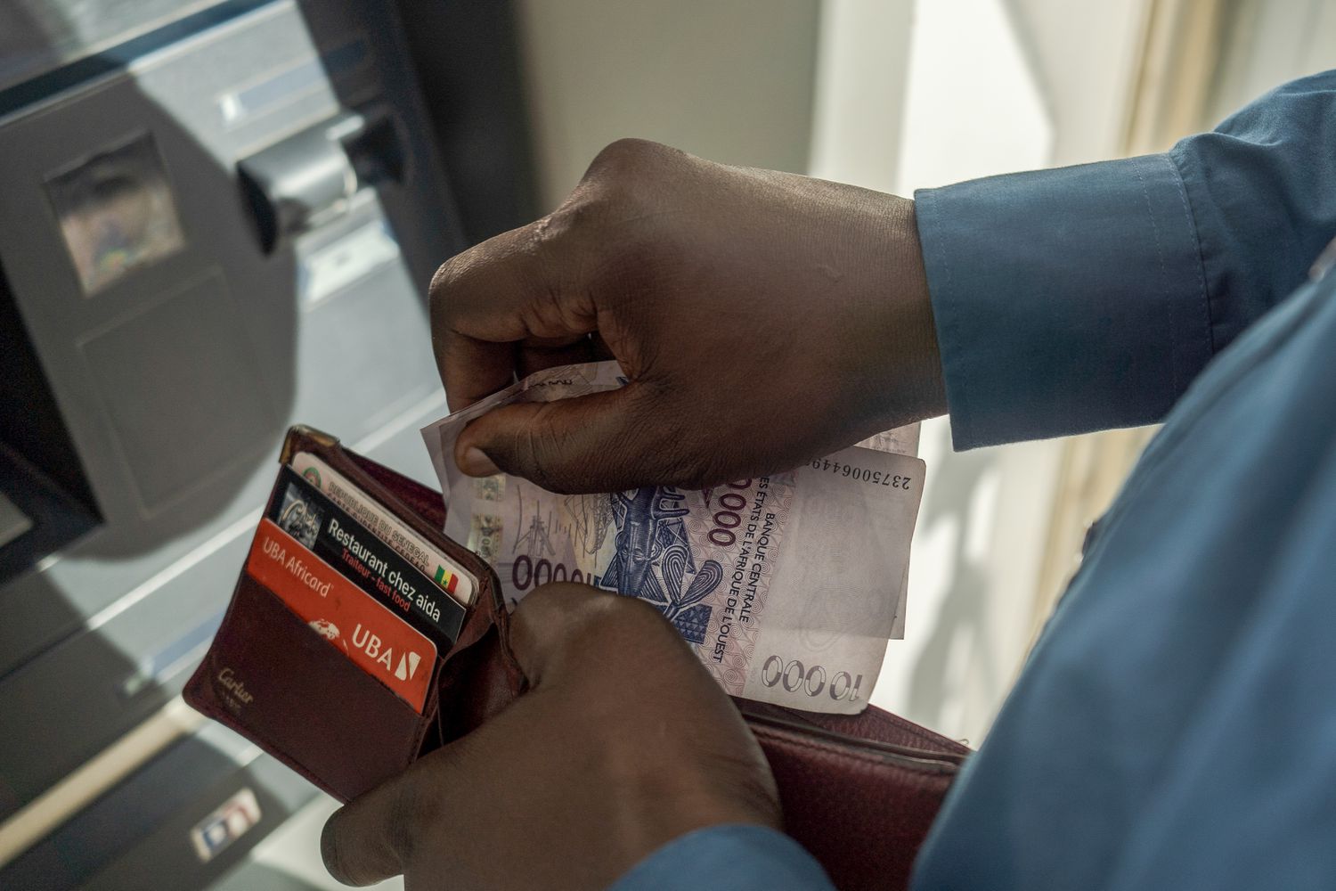 A bank customer withdraws West African Franc banknotes from an automated teller machine.
