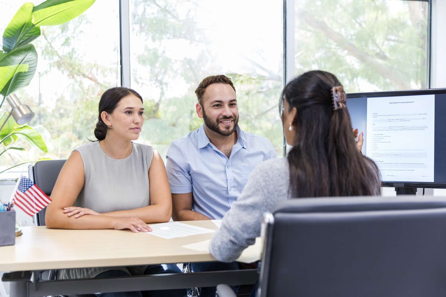 A young couple sit at a table at a credit union, listening to an employee.