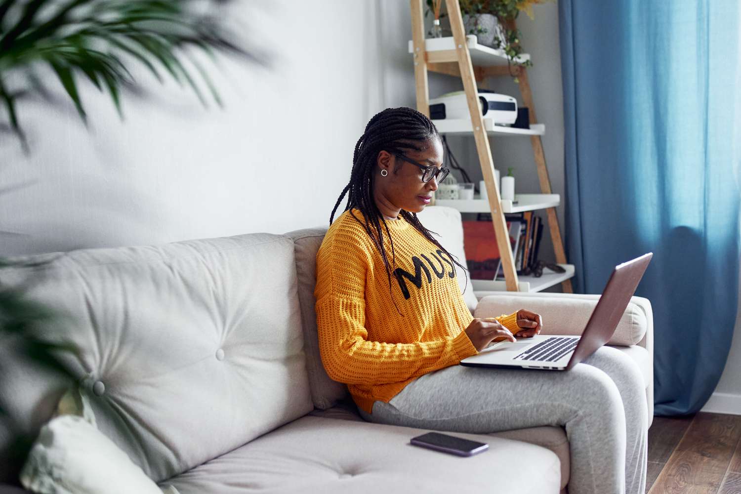 Young Black woman looking at laptop while sitting on sofa.