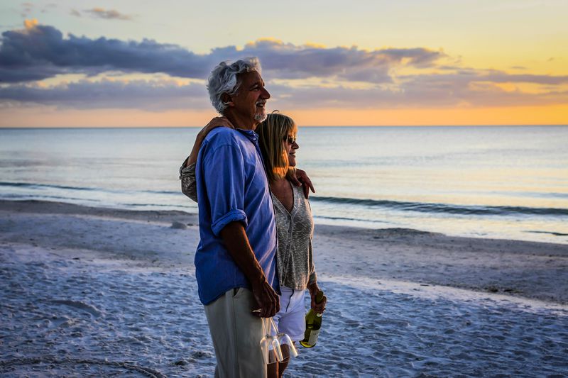 Retired couple enjoy a romantic interlude with a bottle of wine and two glasses at sunset on Siesta Key beach Florida.