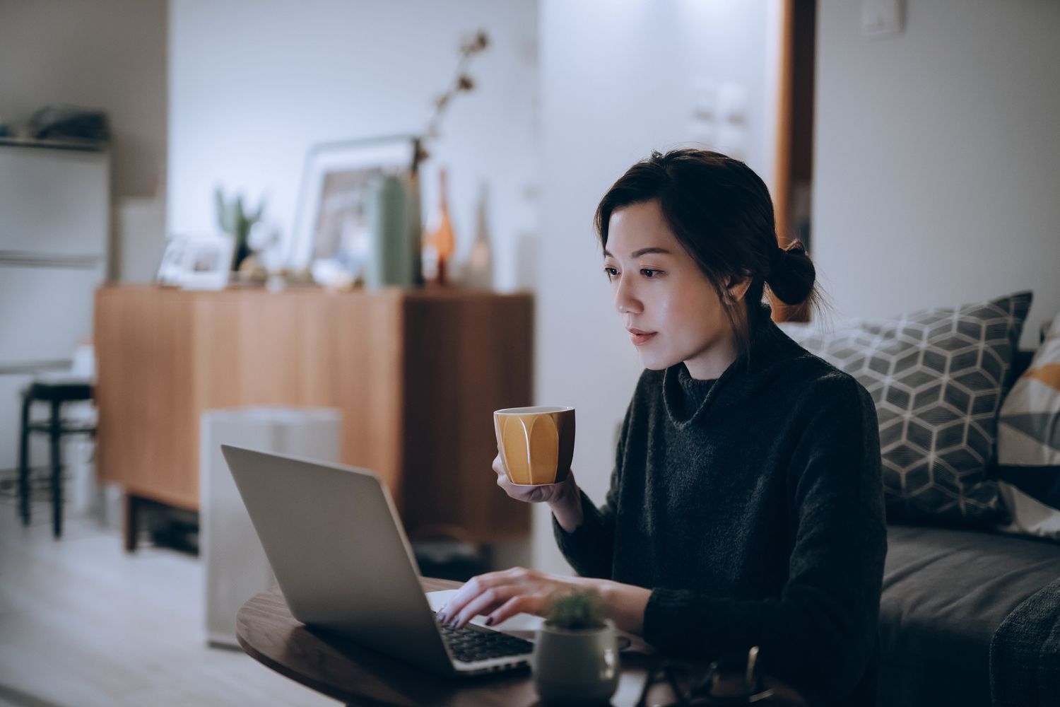 A woman holds a coffee mug and types on a computer.