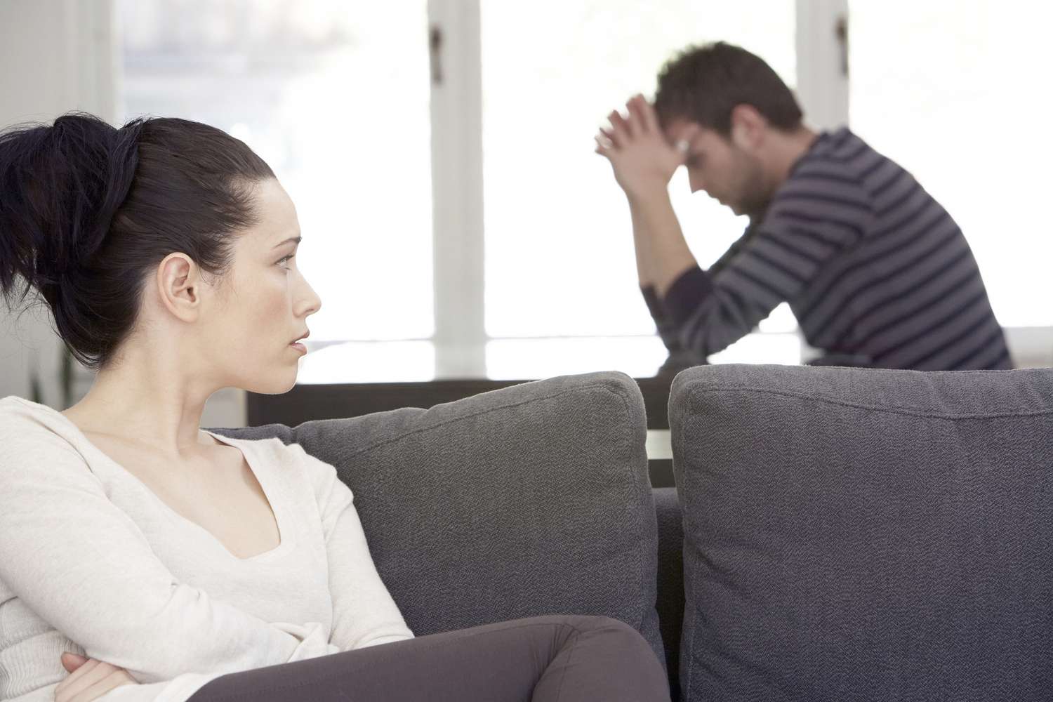 Couple looking distressed while woman sits on a couch and man holds his hands over his head.