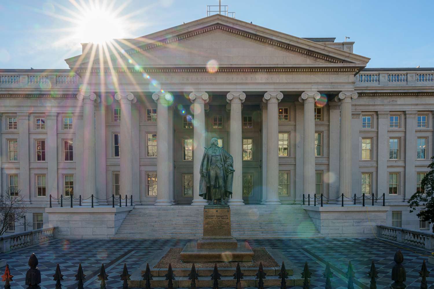 The sun flares over the headquarters of the U.S. Treasury on Jan. 3, 2024, in Washington, D.C. A statue of former Secretary of the Treasury Albert Gallatin sits in the courtyard.
