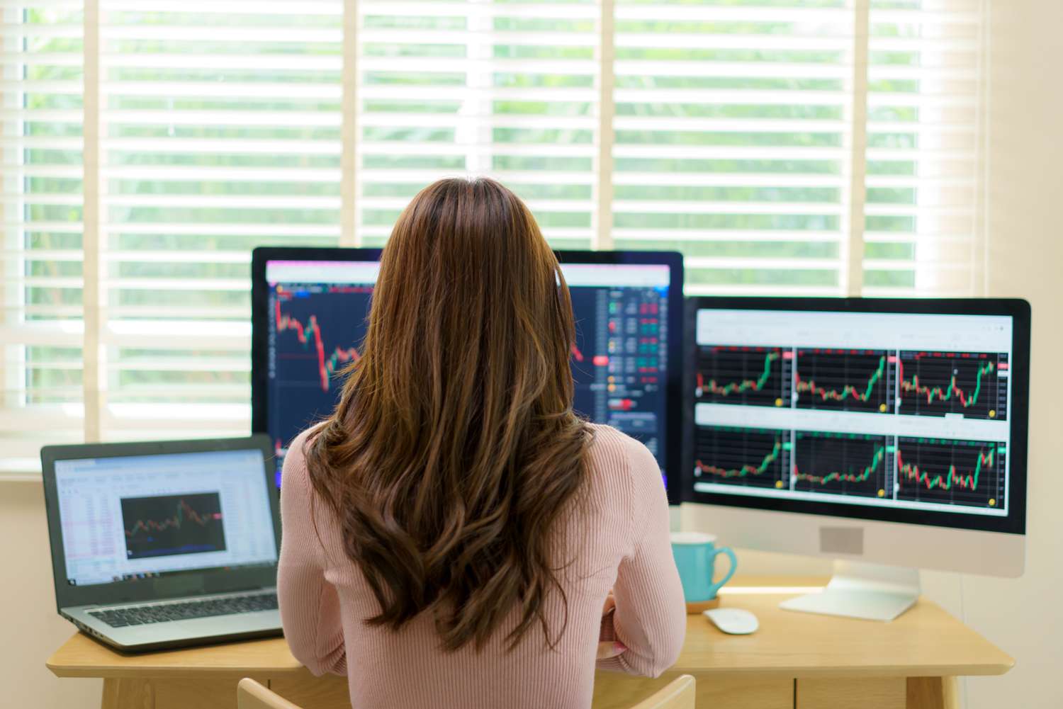 An investor sits at a desk with several computer monitors displaying trending data for the stocks they follow.