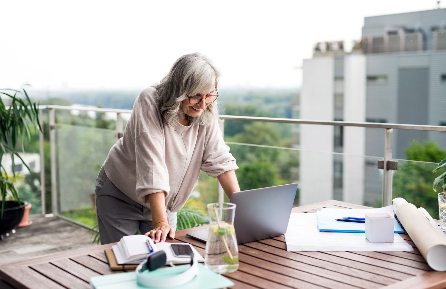 A woman uses a laptop on an outdoor table surrounded by work materials, overlooking an urban setting.