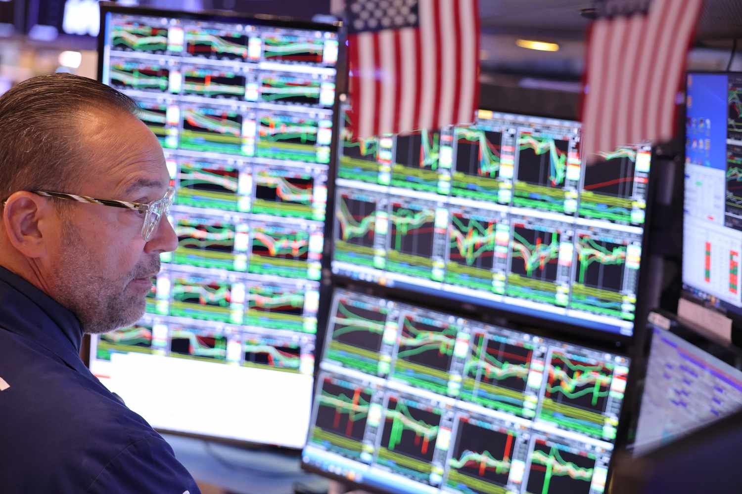 A trader looks at multiple computer screens depicting trading charts on the floor of the New York Stock Exchange. 