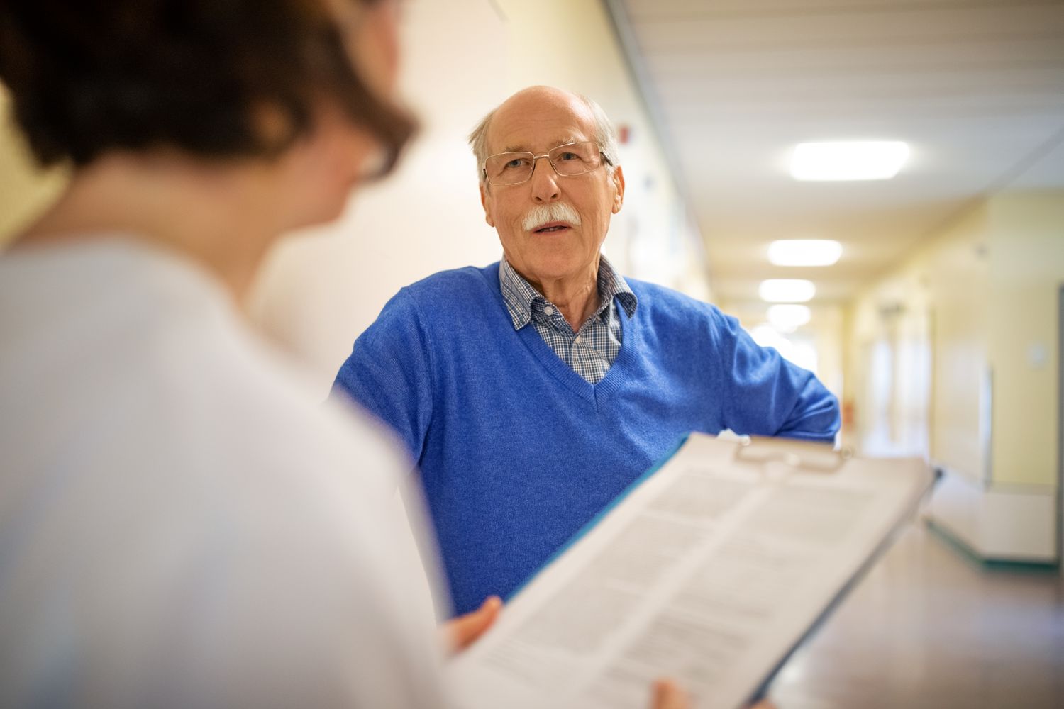 A senior man talks with a doctor in a hospital hallway.