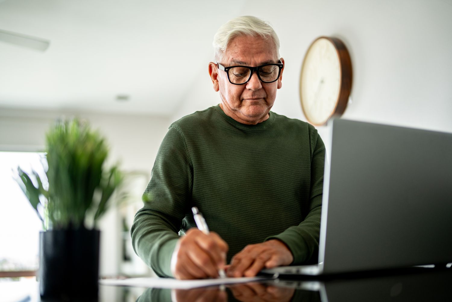 Older man writing on paper next to a computer