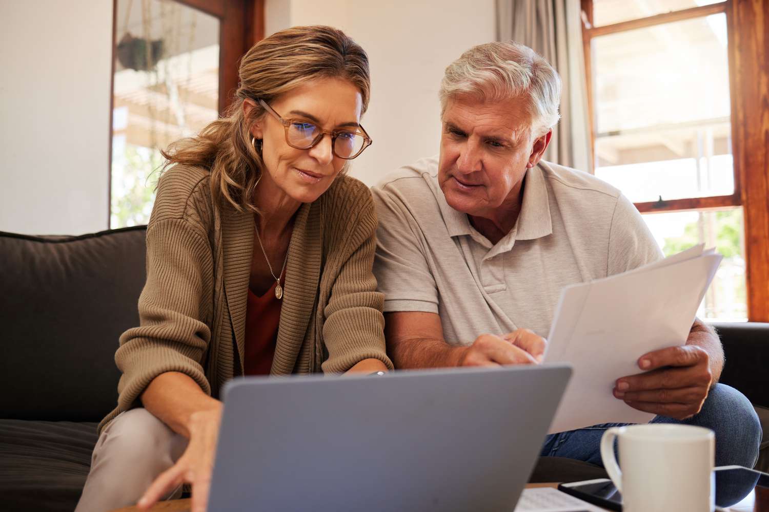 Older couple sitting on their sofa as they look at mortgage documents and a laptop