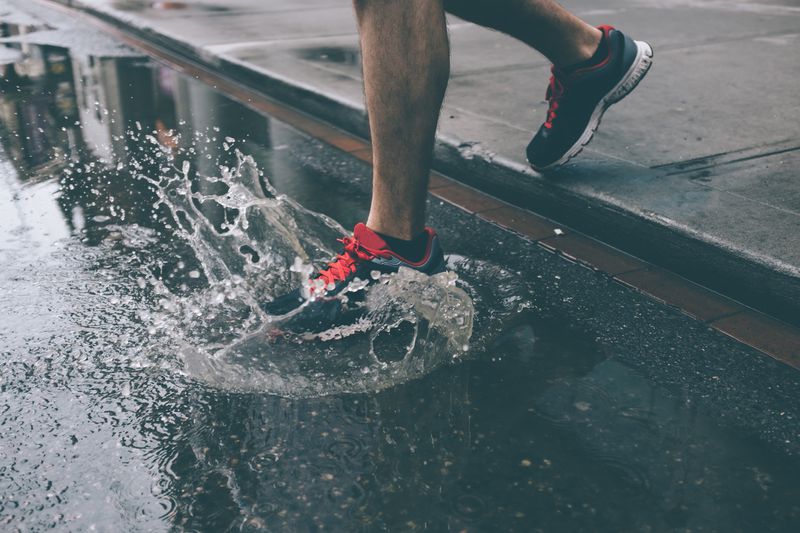 Below-knee view of a person running with sneakers and their foot splashing in a street puddle