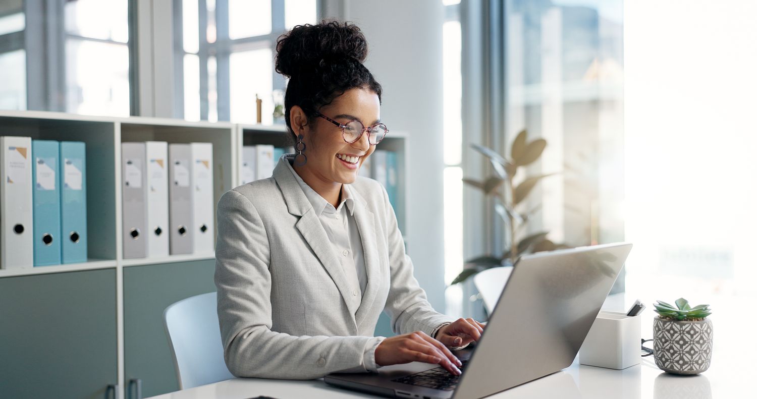 Woman typing on a laptop in an office setting with open and airy windows.