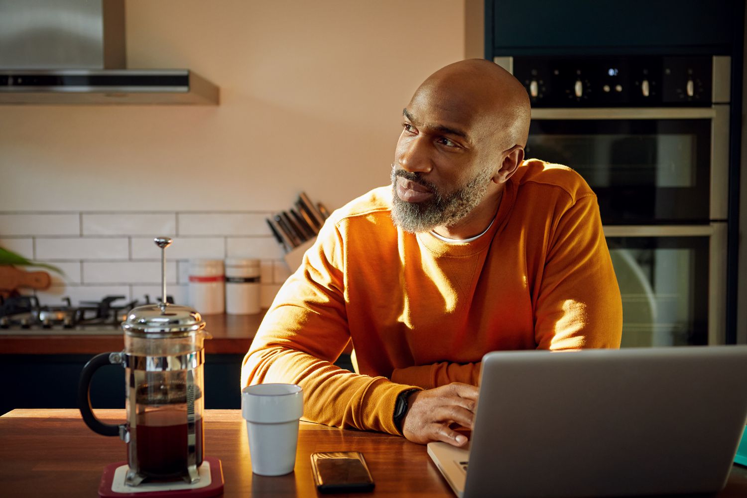 A man in a kitchen with a laptop computer and coffee