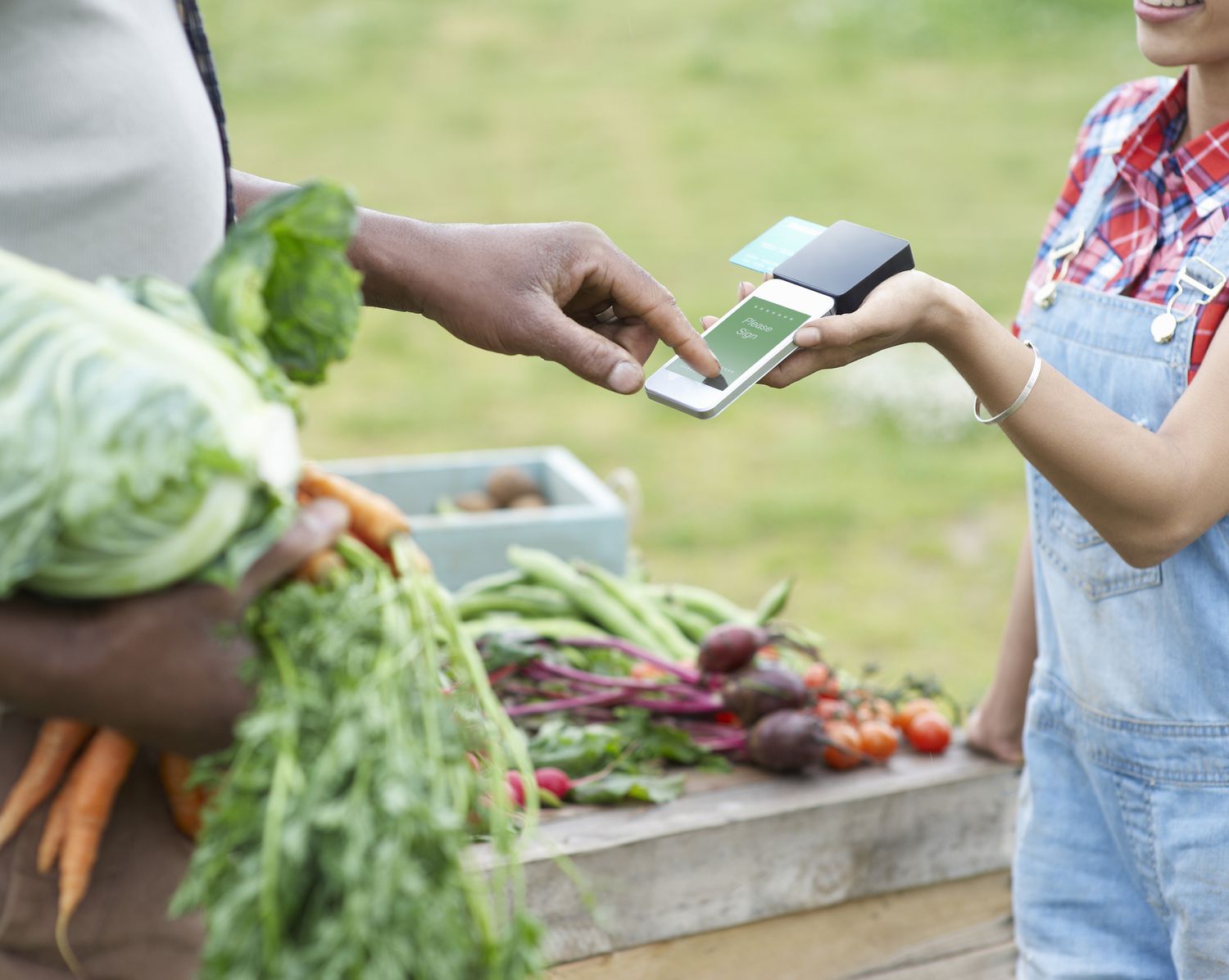 A man pays a woman for some vegetables using a mobile payment device.