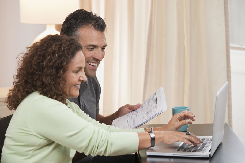 Couple sitting beside each other pay taxes using a laptop