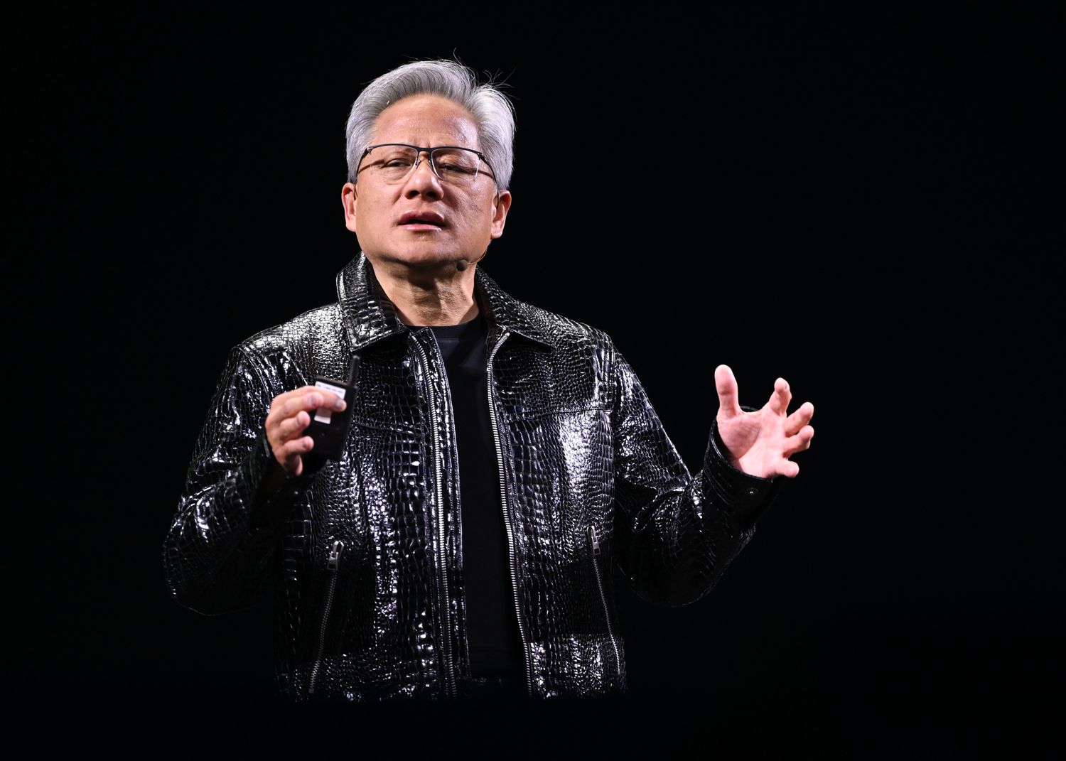 Nvidia CEO Jensen Huang stands speaking on stage in front of a black screen background,