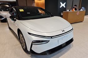 A white XPeng G6 car in a showroom, with a person sitting behind a desk to the right of the car