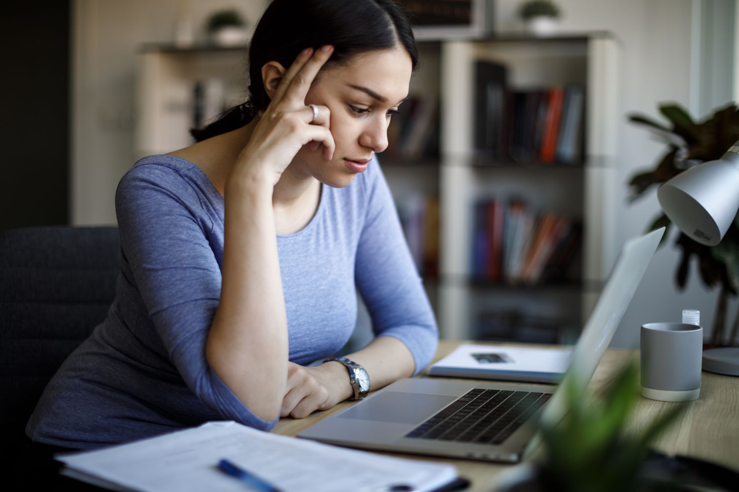 Young woman at home looking intently at her laptop and financial documents