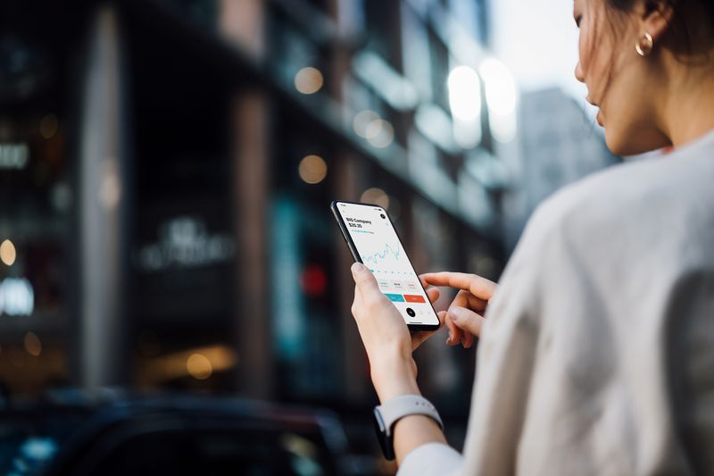 Over the shoulder view of a woman looking at her smartphone with financial data on it