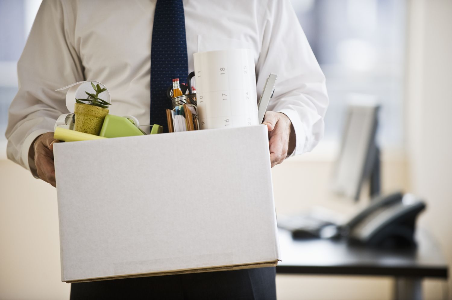 An employee who has been laid off caries a box of their personal belongings out of their office.