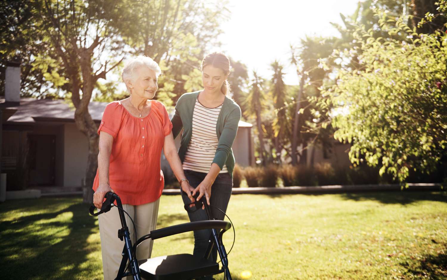 A retiree uses a walker with the help of an aide