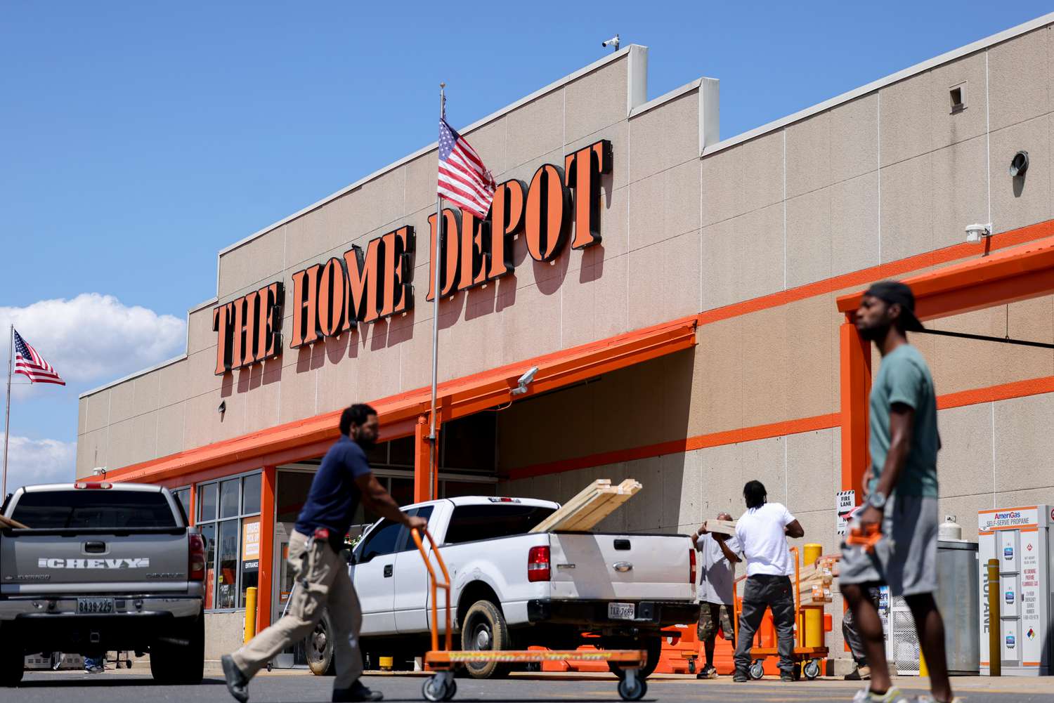 People and two trucks are in front of a Home Depot store with an American flag flying 